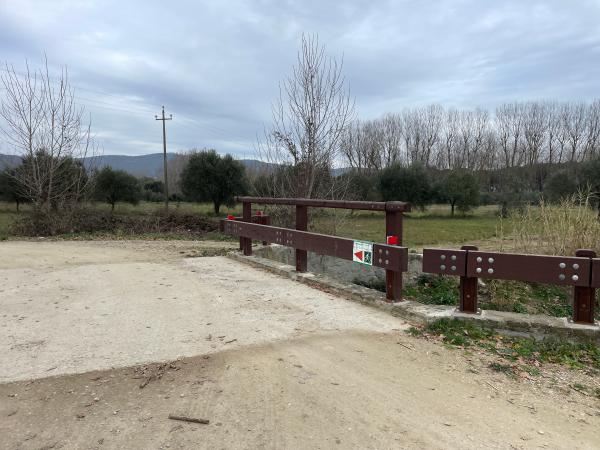 Une barrière marron marque un pont en béton au-dessus de la piste cyclable. Un panneau vert et blanc indique la direction aux cyclistes.